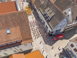 Street photographed from above during a parade. People in colourful costumes, old roofs and