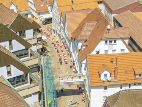 Aerial view of people moving through narrow streets of a half-timbered town under a bright sun, 950
