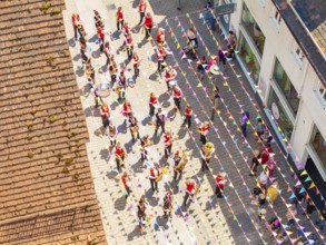 Parade with people in colourful outfits on a street decorated with flags, taken from a bird's eye