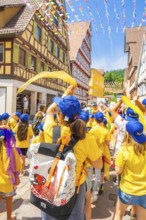 Children in yellow clothing and blue caps waving scarves in a colourful old town, 950 years of