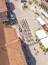 Aerial view of a parade through the alleys of a half-timbered town in sunshine with a crowd of