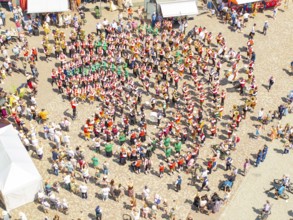 Aerial view of a festive parade on a town square with traditional costumes and a band, 950 years of