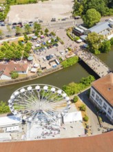 Aerial view of a Ferris wheel near a river with neighbouring town market and people in summer mood,