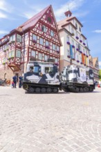 Military vehicles in front of a historic half-timbered building in a sunny old town, 950 years of