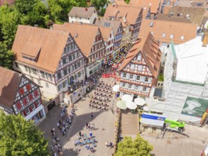 Aerial view of a town square surrounded by half-timbered houses with many people at a celebration,
