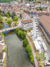 Aerial view of a town with a river, Ferris wheel and surrounding buildings, surrounded by greenery,
