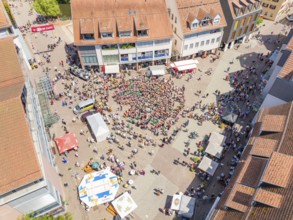 Aerial view of a busy market square with a crowd of people and surrounding buildings in a summer