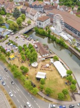 Park event near the city centre with people and Ferris wheel on a river, surrounded by streets, 950