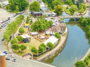 Aerial view of a small park with people, surrounded by a river and city infrastructure, 950 years