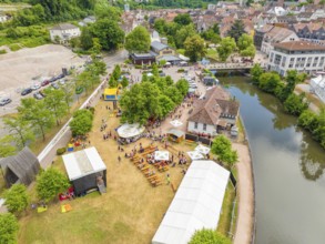 Aerial view of a town festival with people and tents on the riverbank next to historical