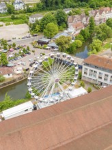 Large Ferris wheel in a park-like area next to a river, surrounded by buildings, 950 years of Calw,