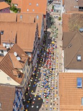 Colourful balloons decorate a busy street, surrounded by houses with red tiled roofs, 950 years of