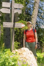 Woman standing at a signpost in nature, surrounded by trees and sunshine, Alpe di Siusi, Dolomites,