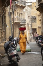 Indian woman carrying a bowl on her head in the old town of Jaisalmer, Rajasthan, India