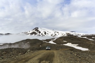 Range Rover drives through volcanic landscape with snow remains, off-road vehicle on gravel track