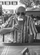 Senior with sunglasses drinking a wheat beer in a beer garden, black and white, Upper Bavaria,