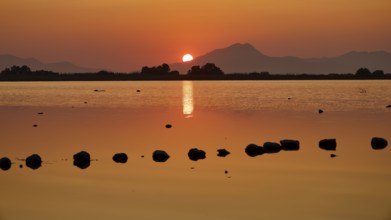 Warm sunset light reflected in the calm lake with mountain backdrop, salt lake, Tigaki, nature