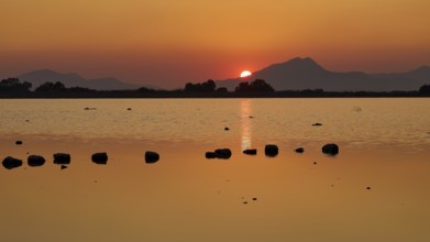 Idyllic scene with setting sun behind a lake and mountains, salt lake, Tigaki, nature reserve,