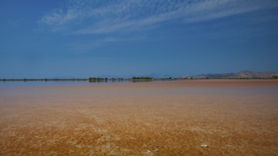Wide, open landscape with a lake under a narrow blue sky, quiet atmosphere, salt lake, Tigaki,
