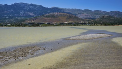 A lake with a long gravel bank and mountains in the background under a blue sky, salt lake, Tigaki,