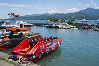 A red jet boat in the foreground of a harbor surrounded by other boats and mountains in the