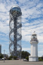 A tall spiral tower next to a white lighthouse under cloudy sky, Alphabetic Tower, Georgian