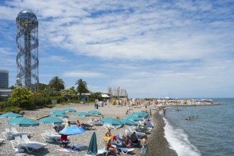Beach with many visitors under umbrellas, a view of the sea and a distinctive tower in the