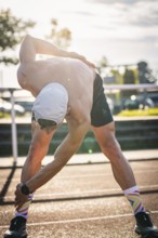Man stretches intensively in sporty clothing in sunlight on a running track, triathlon, Calw,
