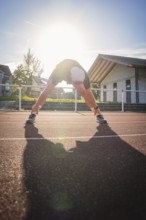 Runner stretching on a running track in strong sunlight early in the morning, Triathlon, Calw,