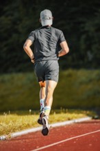 Person running on red covering in grey sports dress in daylight, triathlon, Calw, Germany