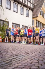 Group of runners at the starting line on a paved road in front of timber-framed houses, triathlon,