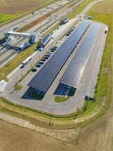 Large parking lot with solar panels along a road and fields, photographed from the air, e-charging