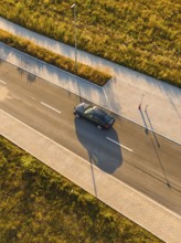 Aerial view of moving car and long shadows on paved road, BMW i7 electric car, deer e-car sharing,