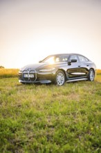 Black electric car in a meadow at sunset, the light falls on the car surrounded by green, BMW i7