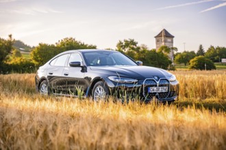 Black electric car in a cornfield, a tower in the background, summer landscape at sunset, BMW i7