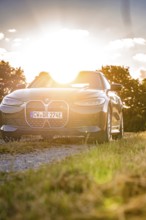 Black electric car on a dirt road in the backlight of the setting sun, atmospheric light-flooded