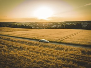 Wide view of a car on a dirt road through gold-colored fields in evening sunlight, BMW i7 electric