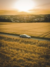 Extensive landscape view of a car on a road through a cornfield at sunset, BMW i7 electric car,