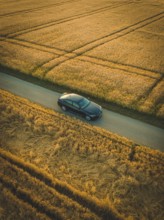 A dark car drives on a paved road surrounded by cornfields at dawn or dusk, BMW i7 electric car,