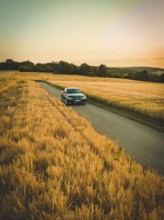Vehicle moving on a country road through vast, golden cornfields in the evening light, BMW i7