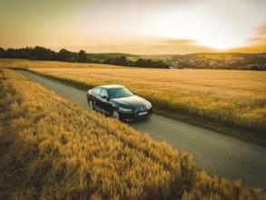 Car driving on a dirt road through golden fields at sunset with rural views, BMW i7 electric car,