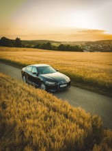 Black car on a country road between wheat fields at sunset, BMW i7 electric car, deer e-car