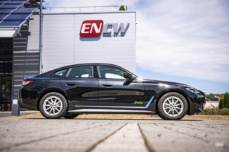 Black car in front of a building with a large company logo under blue sky, BMW i7 electric car,