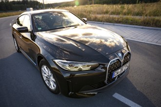 A black car on a road with reflecting sky and a field, BMW i7 electric car, Deer e-Carsharing,