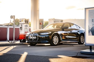Black car at a gas station in the evening sun with modern architecture, BMW i7 electric car, Deer