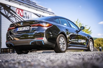 Rear view of a black car in front of a modern building with ENCW logo and blue sky, BMW i7 electric