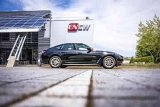 Black car on the side of a modern building with ENCW logo on a paved path, BMW i7 electric car,