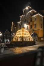 Overview of illuminated fountains in front of traditional buildings in a nocturnal town, Calw,