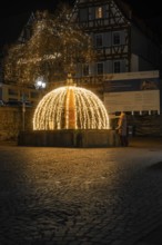 Atmospheric illuminated fountain at night in a paved old town scenario, Calw, Black Forest, Germany
