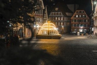 Idyllic night scene with illuminated fountain and traditional buildings in the city center, Calw,